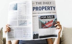Woman reads the newspaper with headlines about the uncertainty of the property market during covid-19.